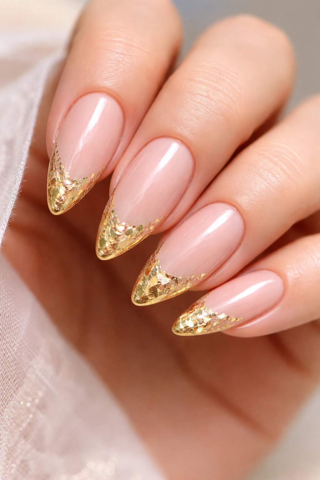 Close-up of almond nails with pale blush base and gold foil tips