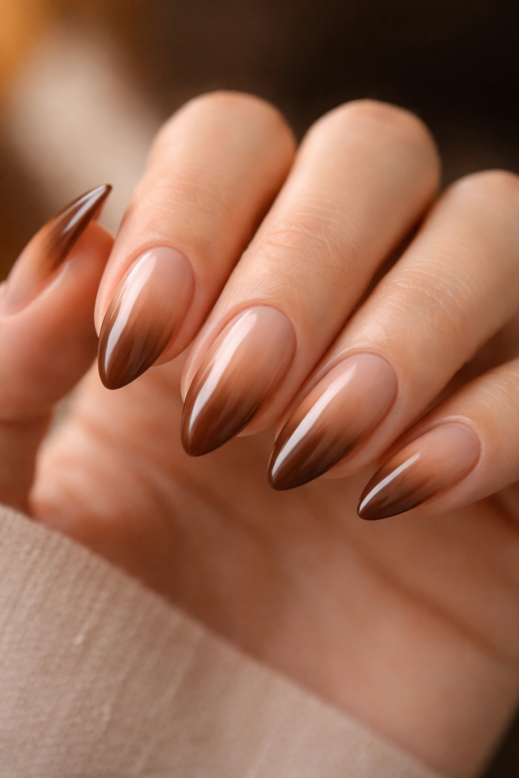 Close-up of almond nails with a warm brown aura glow on nude base