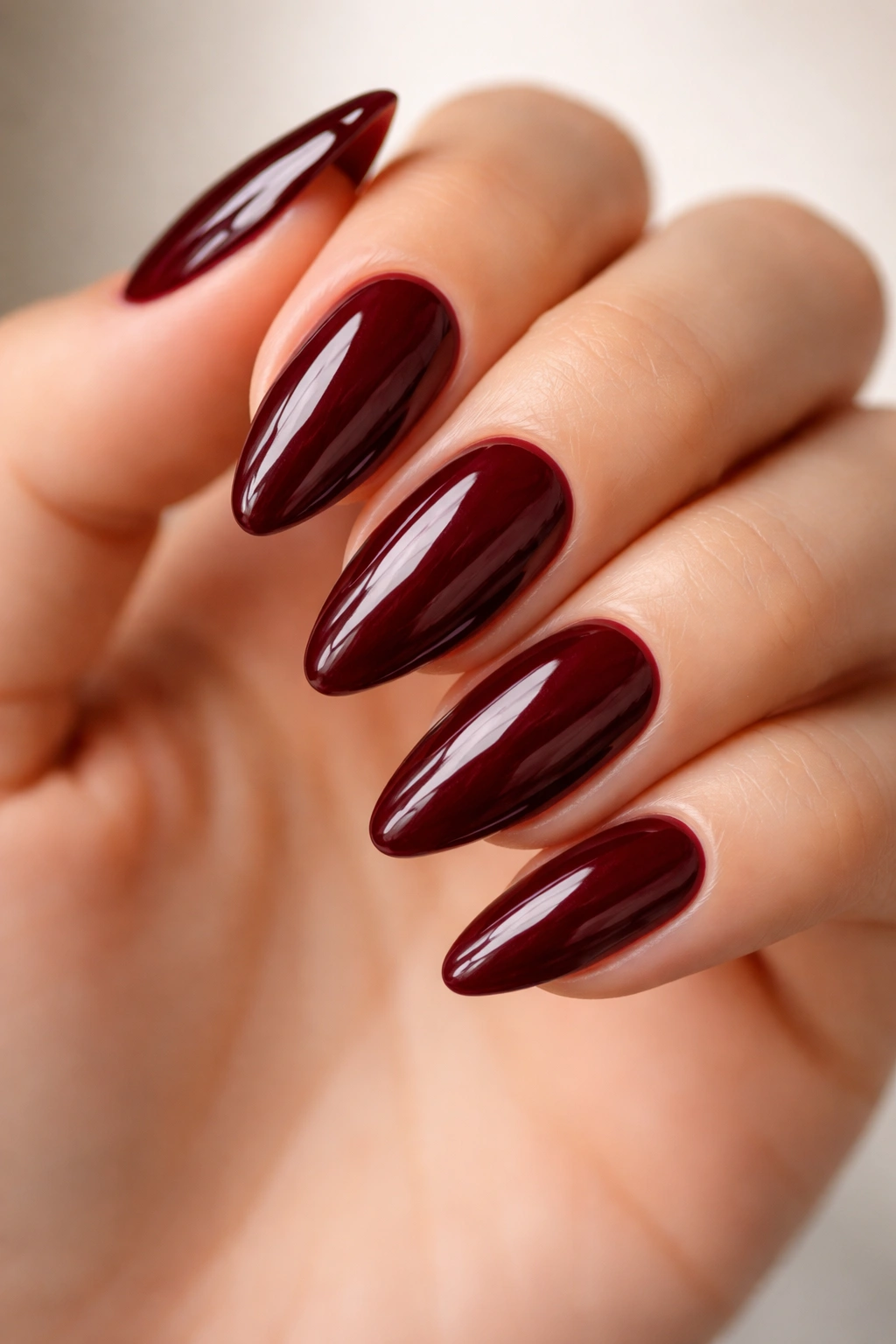 Close-up of high-gloss burgundy almond nails on a bare hand