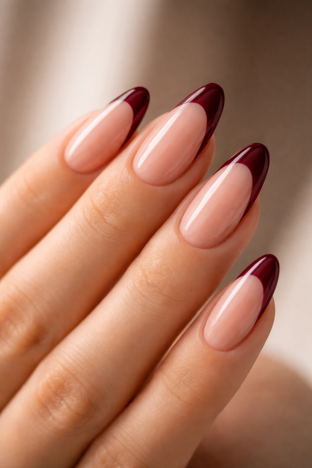 Close-up of almond nails with deep burgundy tips on a nude base.