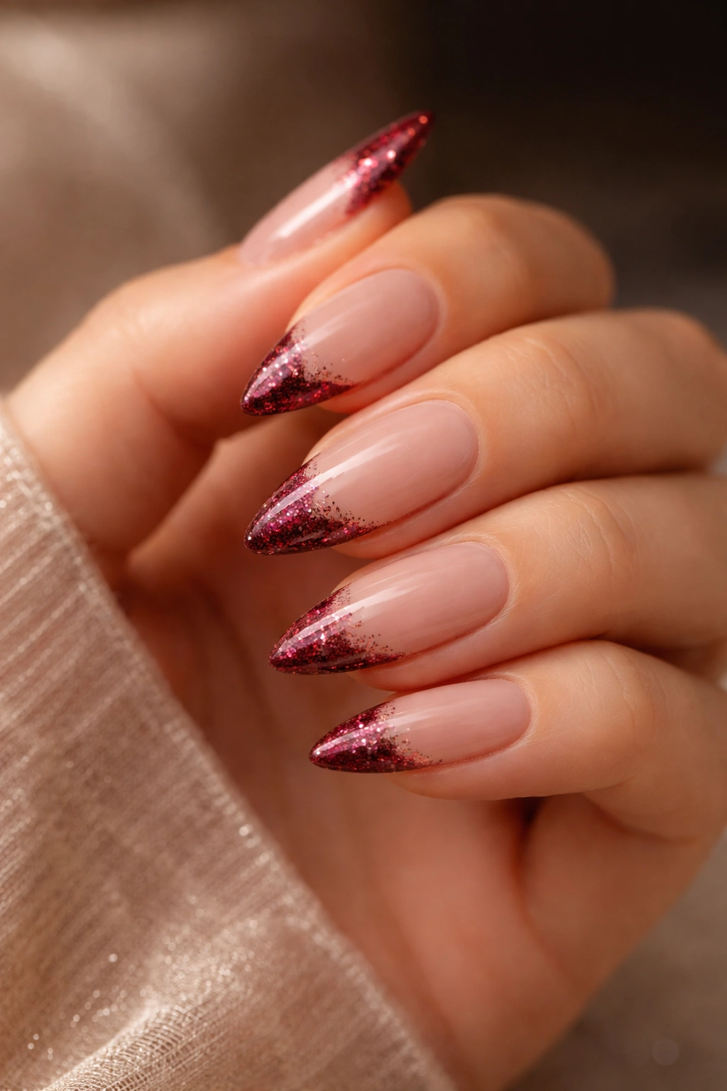 Close-up of burgundy glitter tips on nude almond nails with curved almond shape
