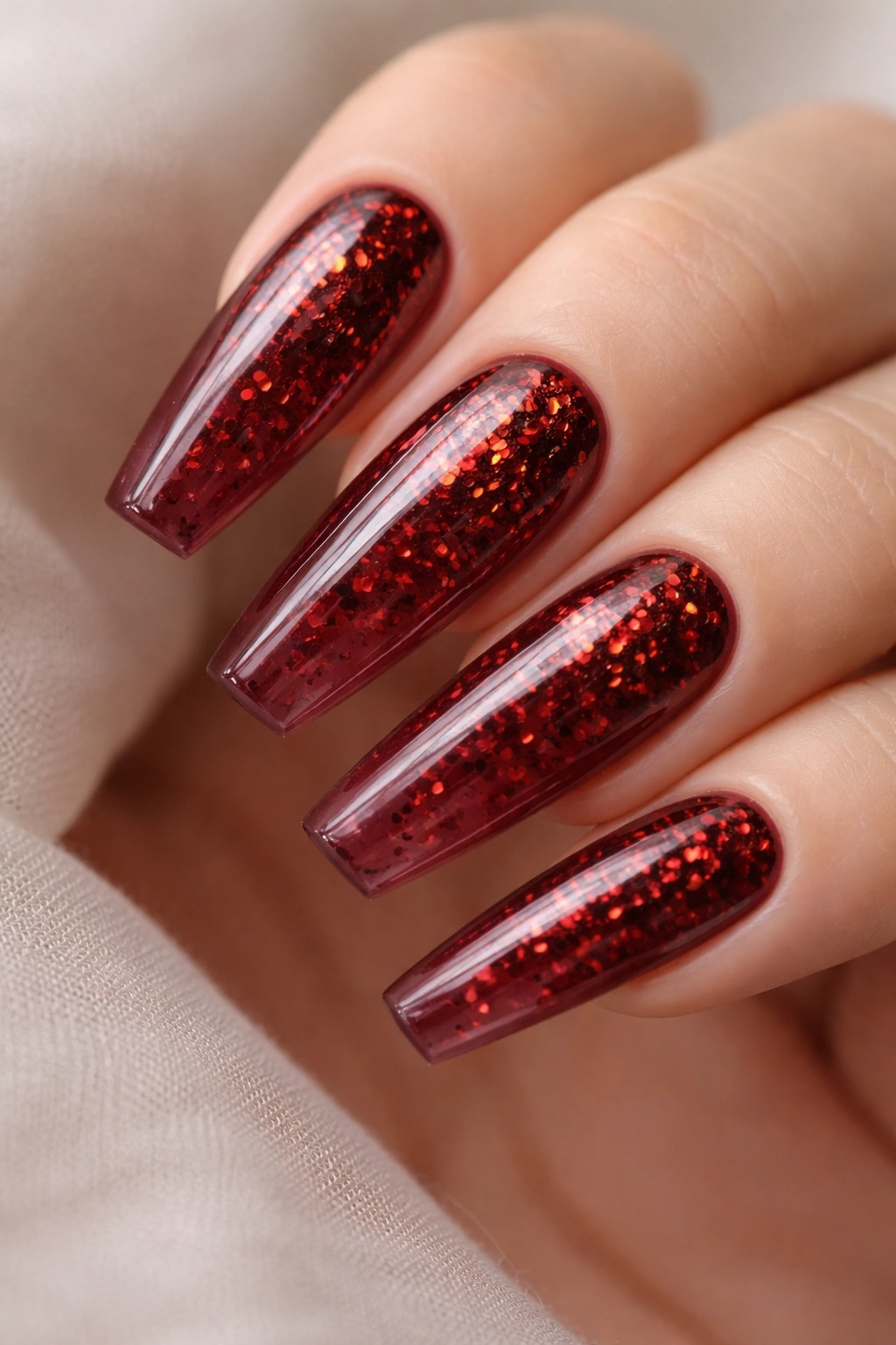 Close-up of burgundy jelly coffin nails with red foil flakes under translucent gel