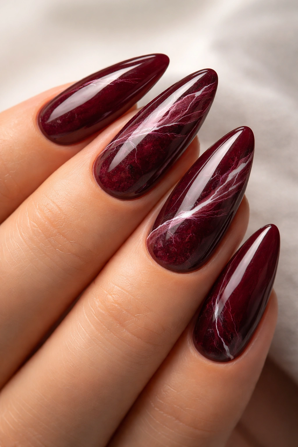 Close-up of burgundy marble nails with white veining on almond nails