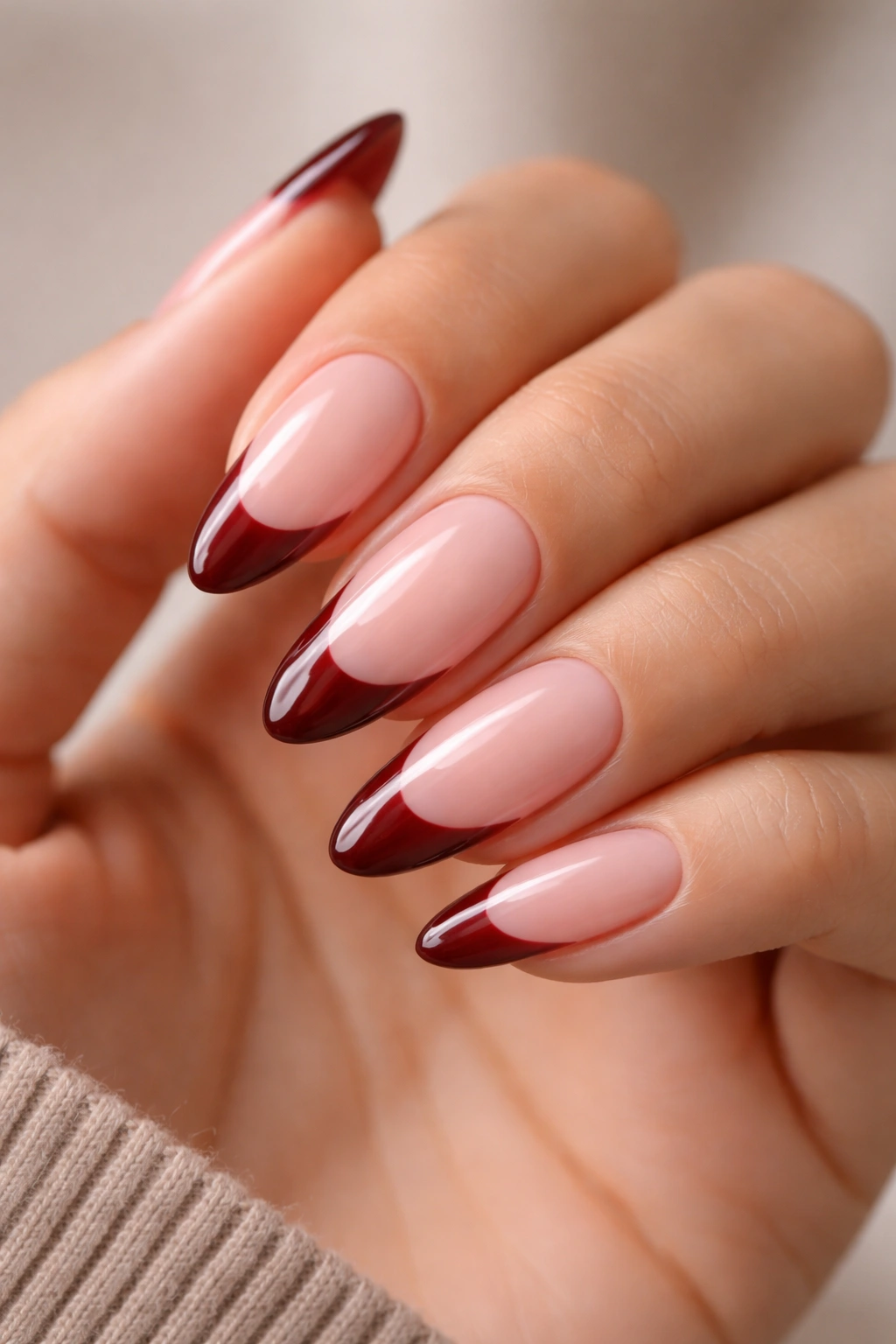 Close-up of almond nails with milky pink base and burgundy tips