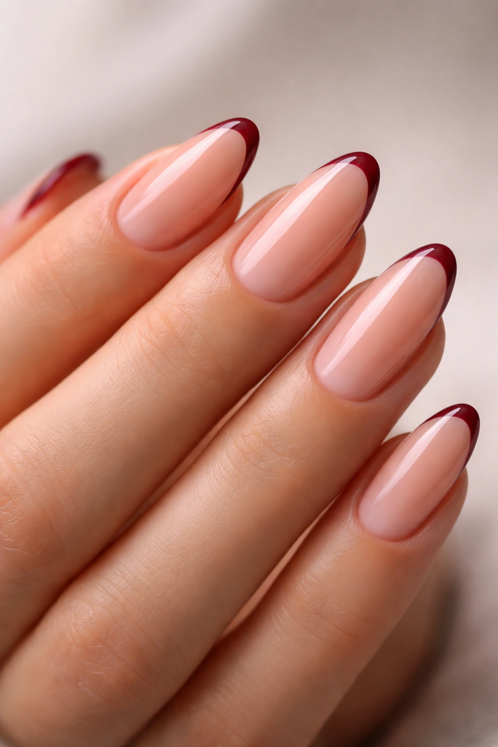 Close-up of deep burgundy almond nails with micro French tips on a sheer base