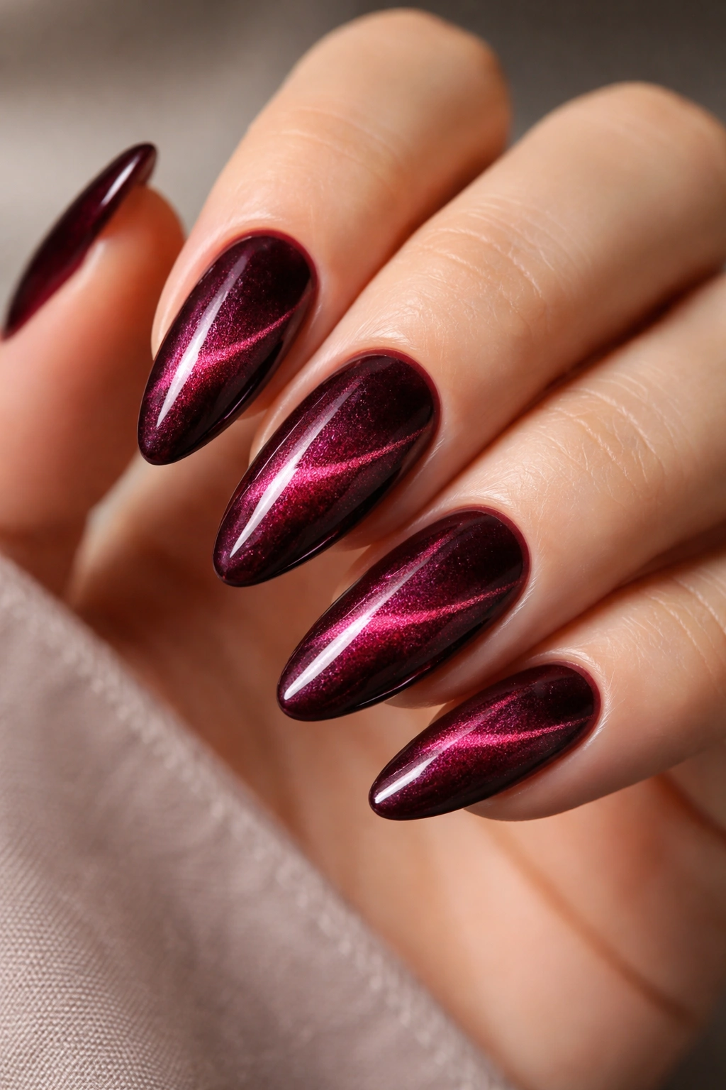 Close-up of burgundy almond nails with velvet cat-eye shimmer and magnetic stripe