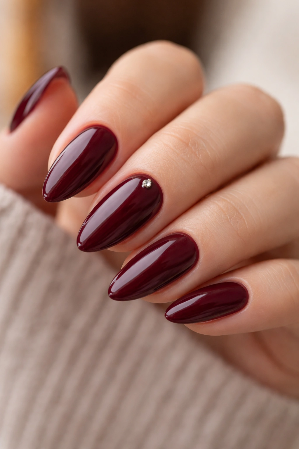 Burgundy almond nails with a tiny gem near the cuticle