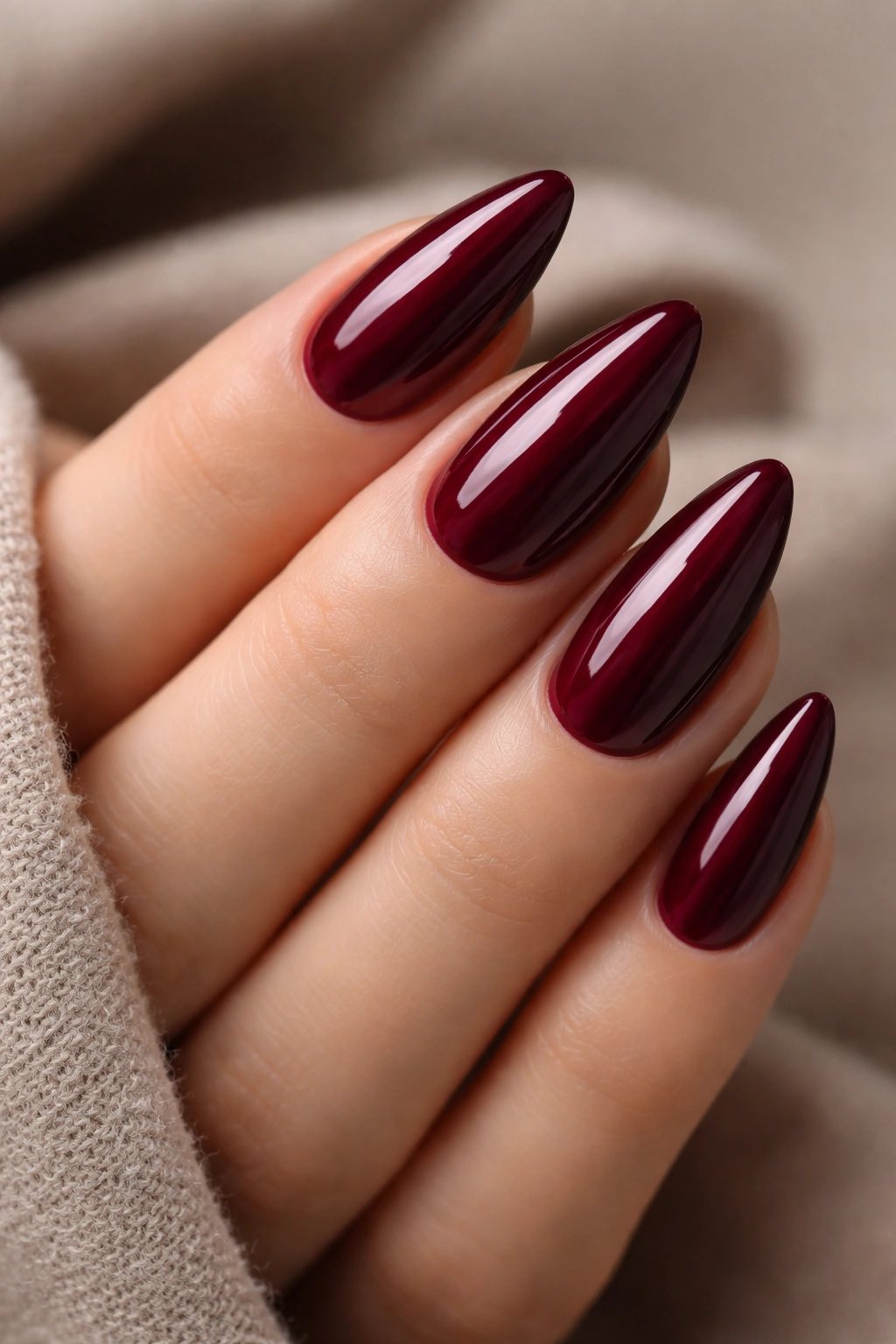 Close-up of glossy burgundy almond nails on a hand with deep wine color and high shine