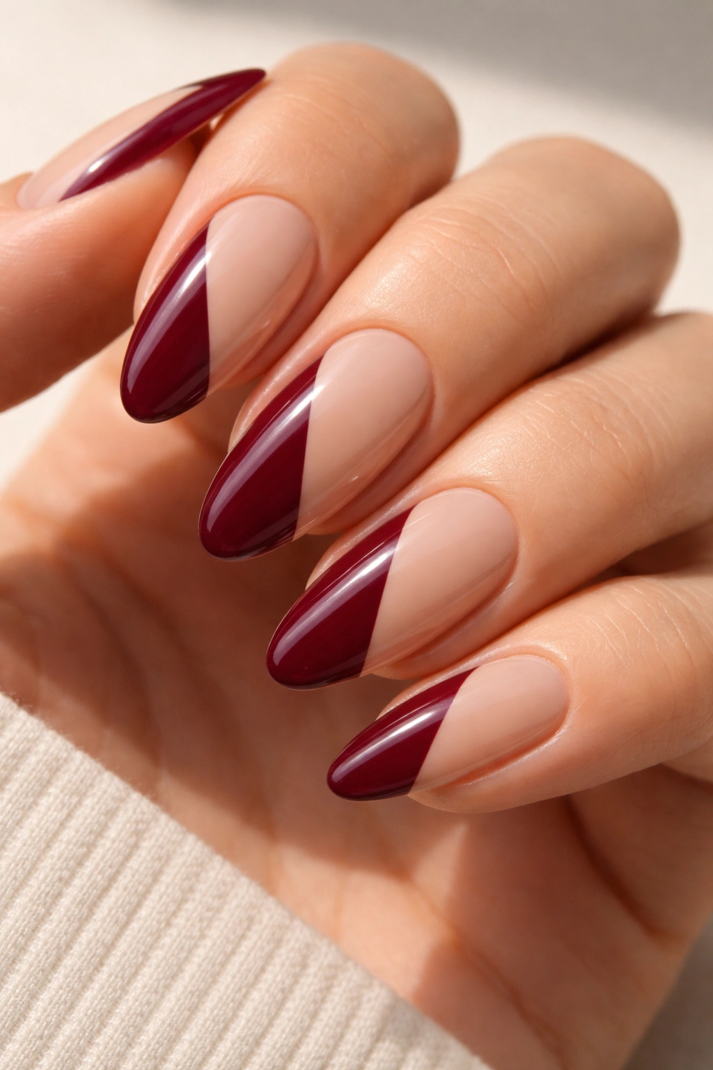Close-up of burgundy and nude color-block almond nails with a diagonal split