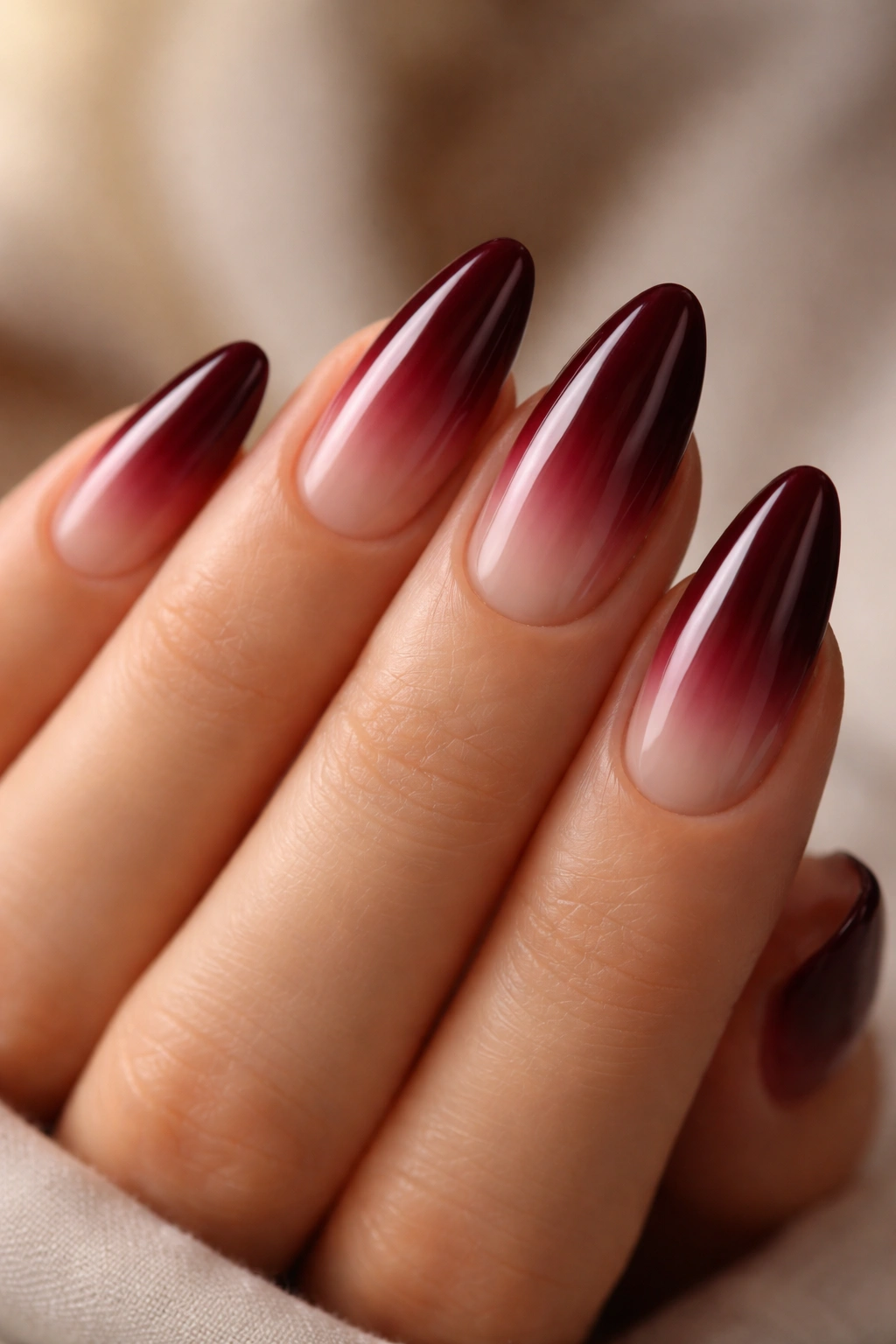 Close-up of deep burgundy ombre almonds nails with nude base
