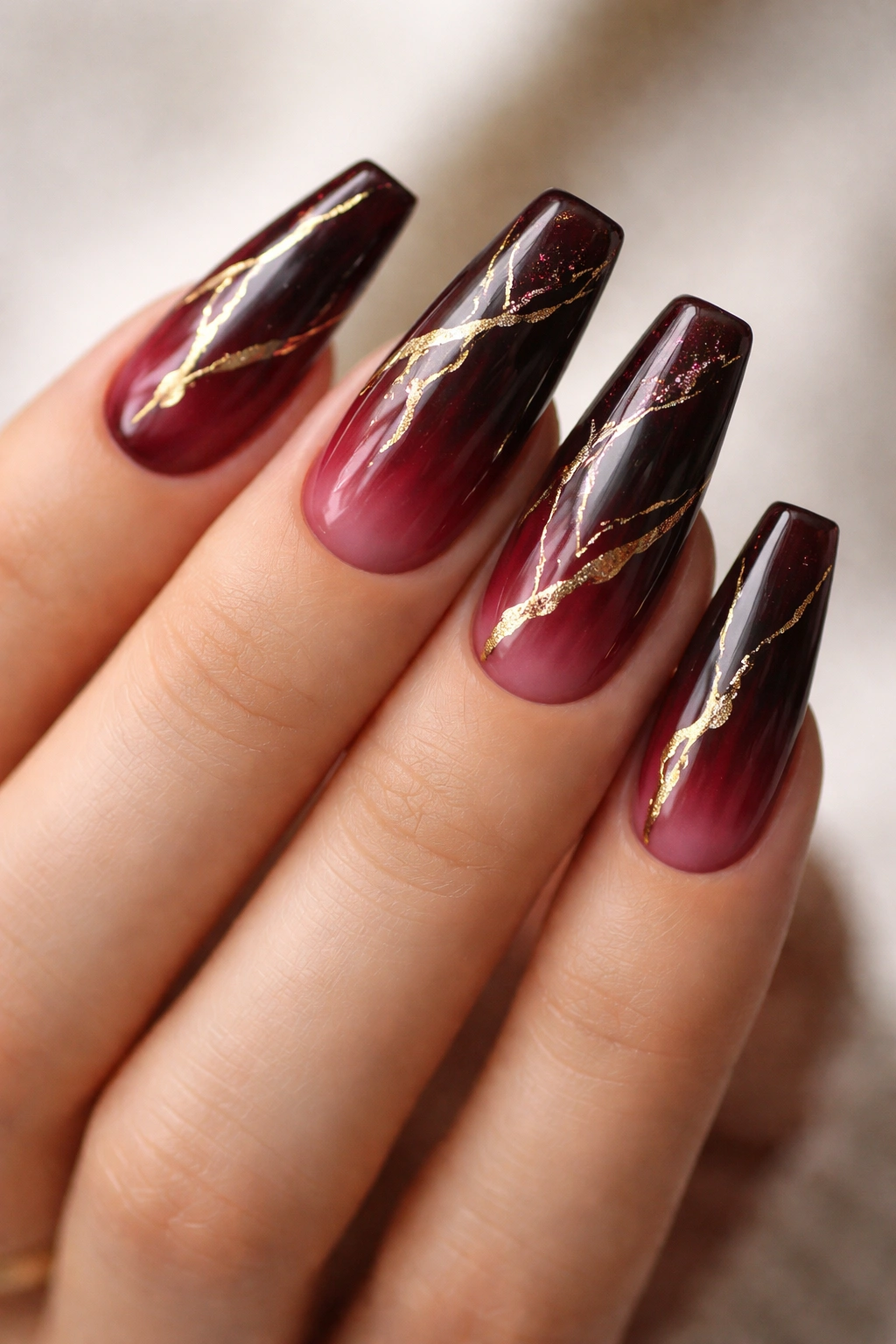 Close-up of burgundy ombre coffin nails with gold veins, photorealistic