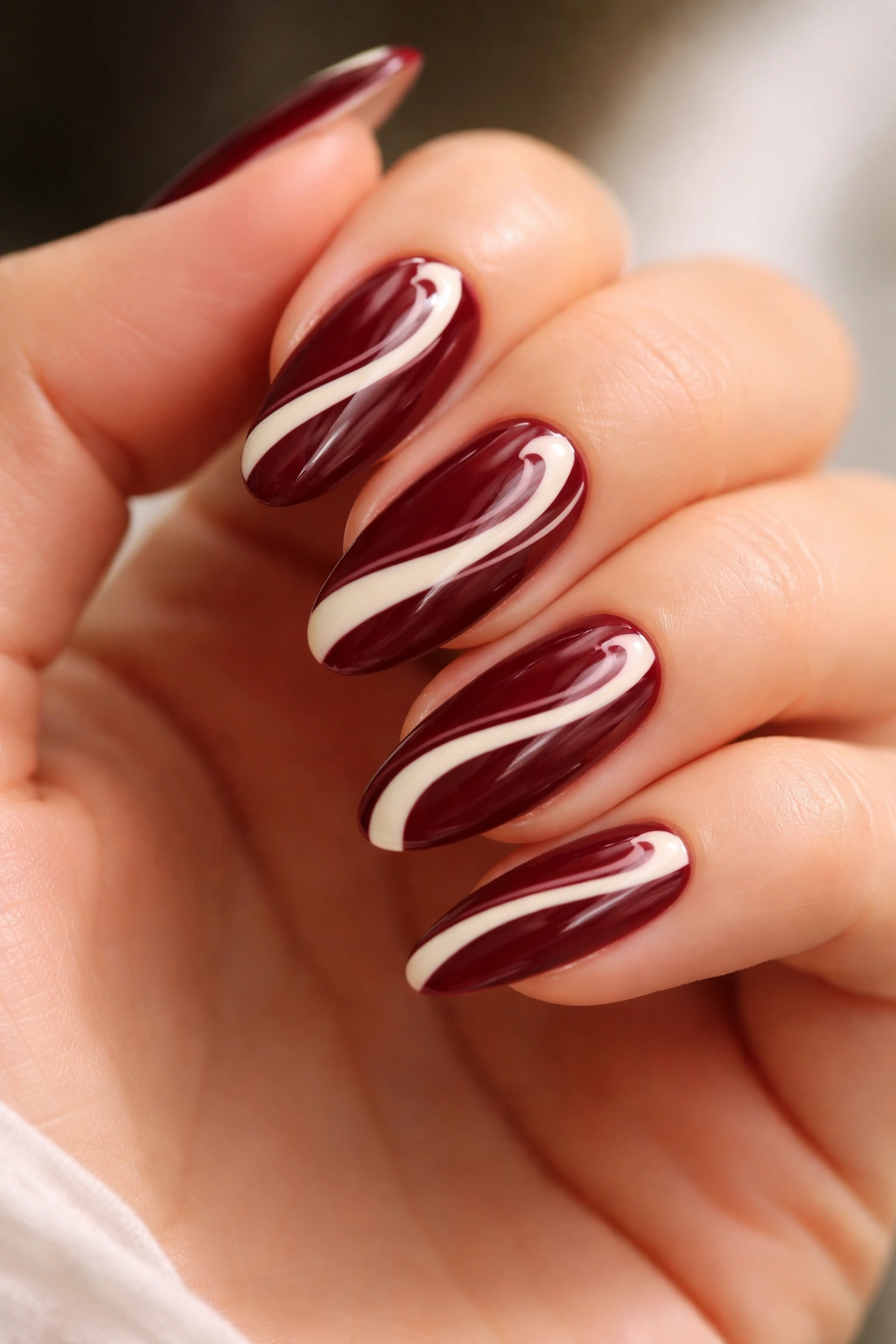 Almond nails with burgundy swirl and cream ribbon lines.