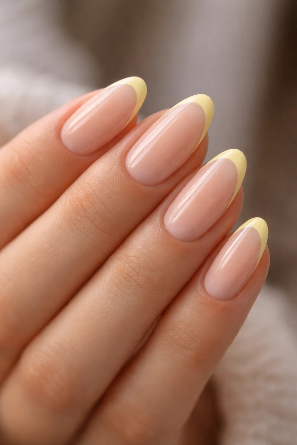 Close-up of almond-shaped nails with sheer nude base and a slim butter-yellow French tip