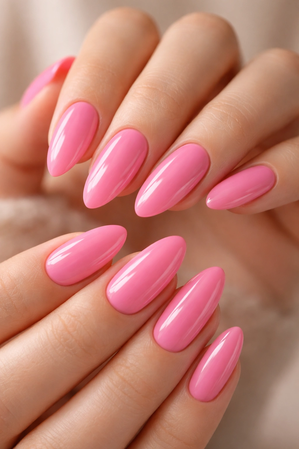 Close-up of almond-shaped nails painted candy pink with a glossy finish