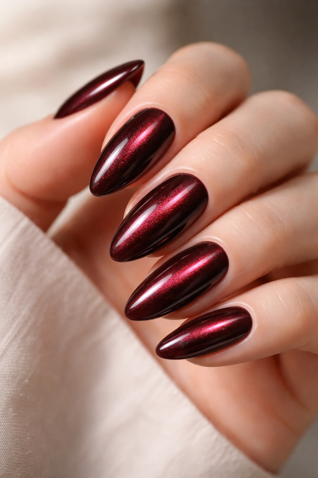 Close-up of almond nails showing cat-eye magnetic line on deep maroon polish.
