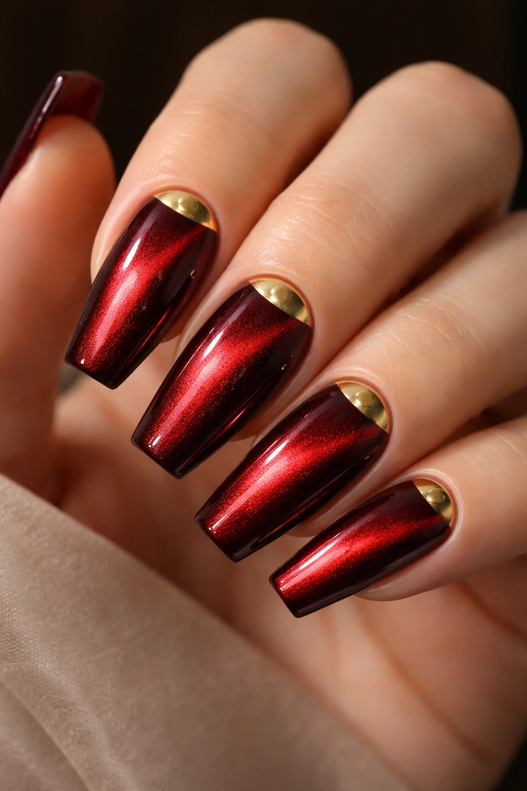 Close-up of metallic red cat-eye nails with gold half moons at the base