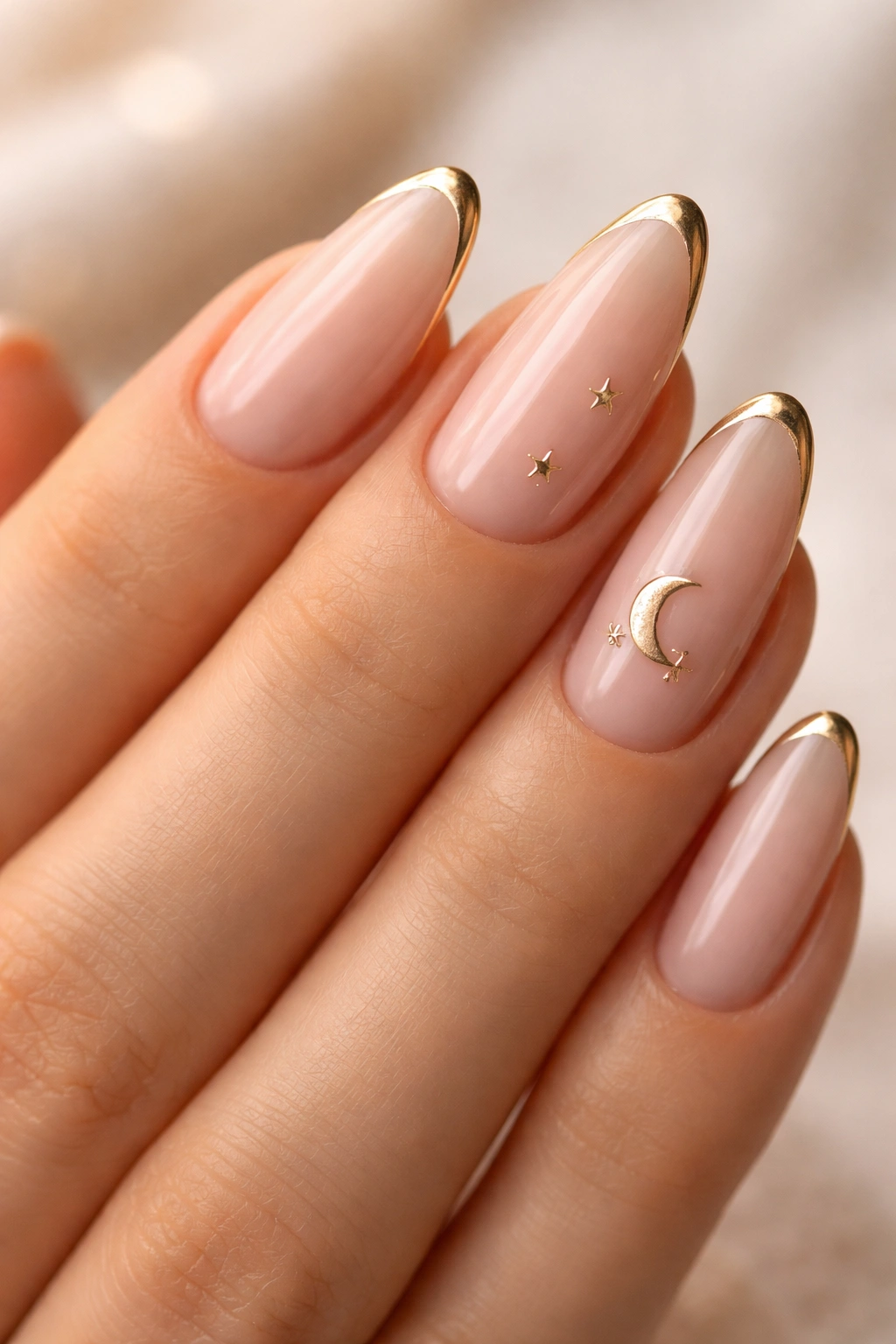 Close-up of almond nails with sheer nude base, gold tips, and tiny star accents