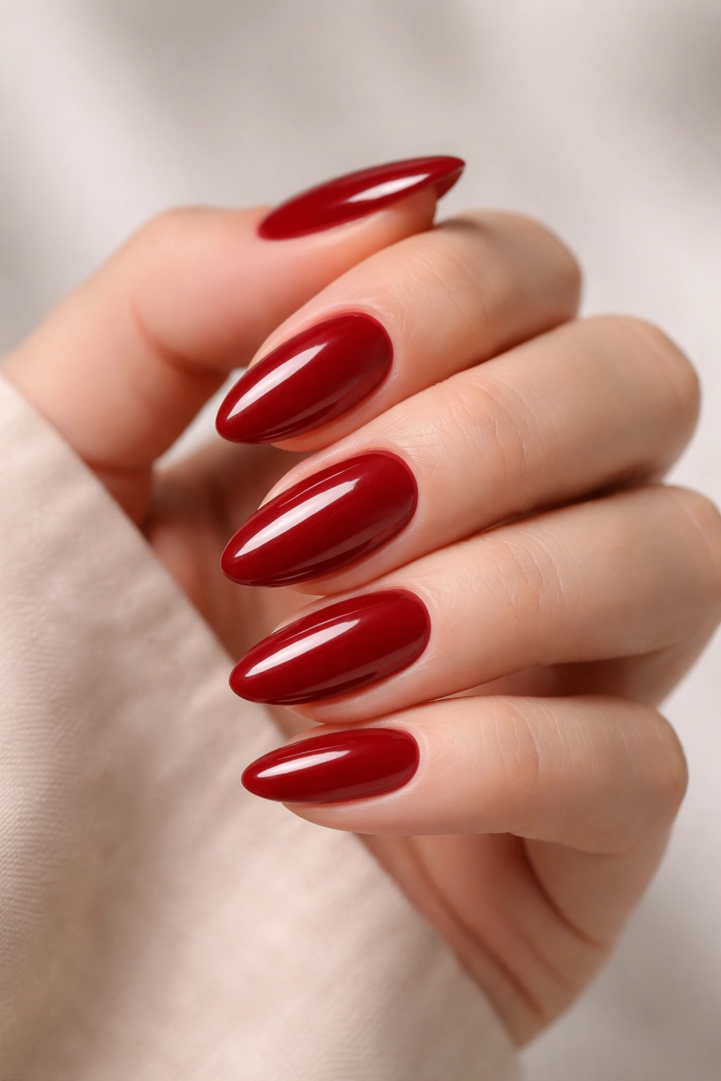 Close-up of classic cherry red almond nails with glossy finish on neutral background