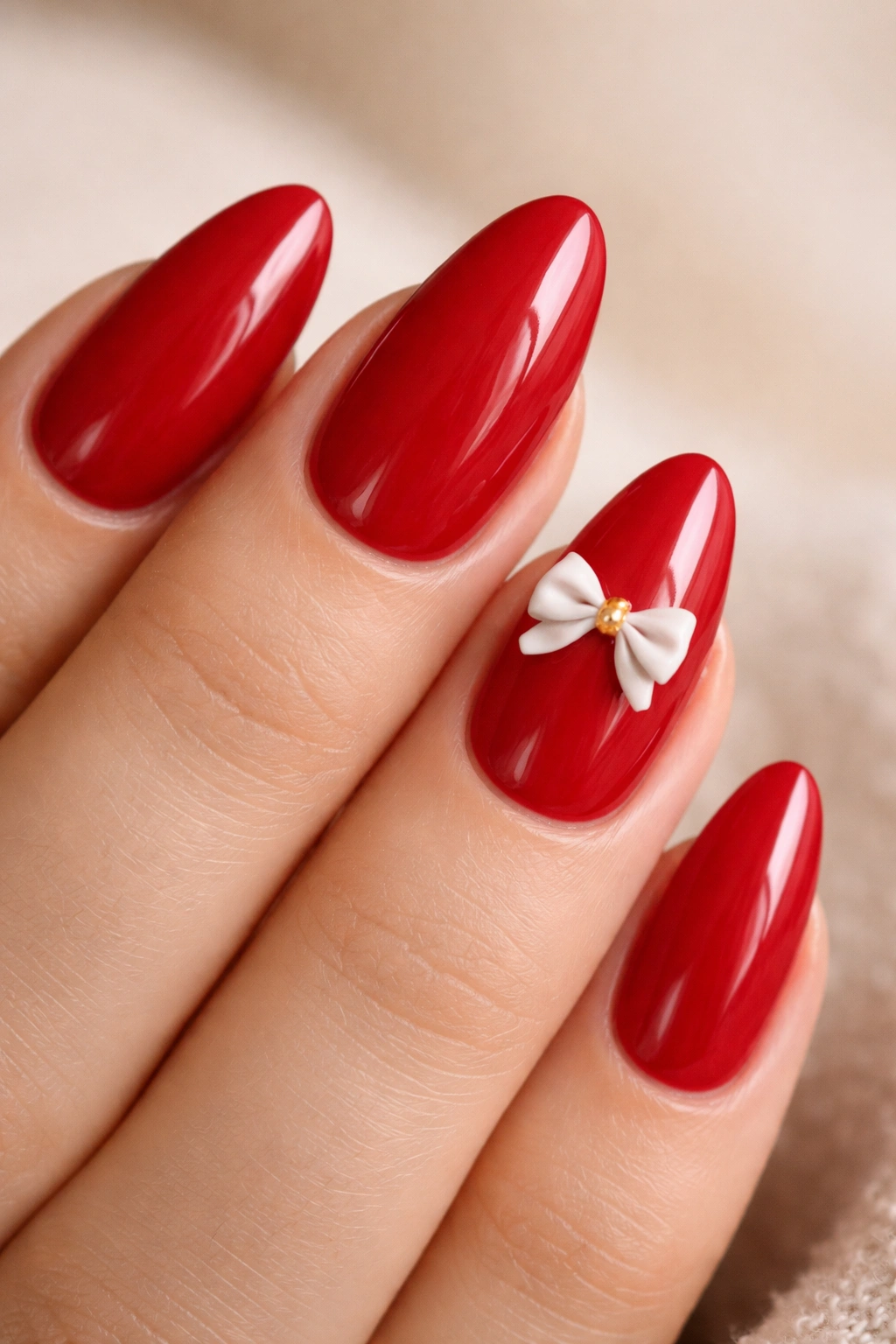 Close-up of almond-shaped cherry red nails with one tiny 3D bow accent near the cuticle
