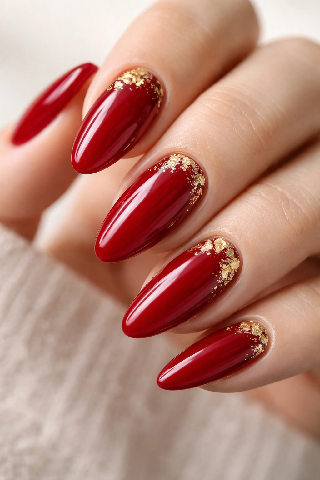 Almond nails with cherry red polish and gold foil accents on neutral background