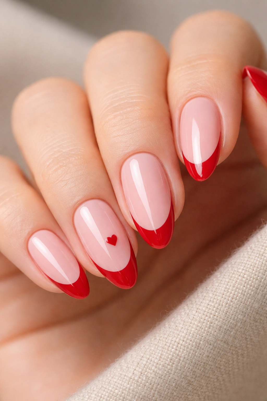 Close-up of almond nails with sheer pink base and cherry red tips, one accent nail with tiny heart.