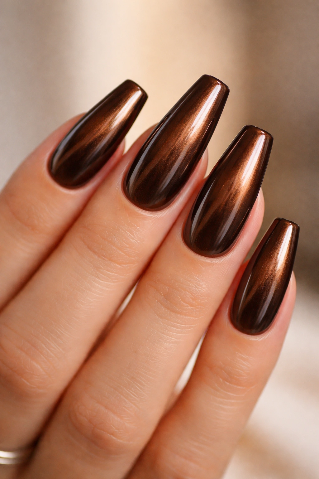 Close-up of deep chocolate brown coffin nails with bronze-gold chrome finish