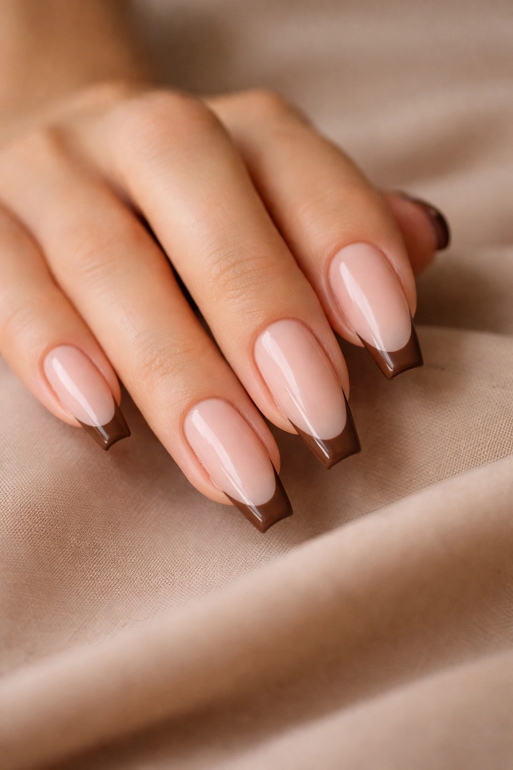 Close-up of chocolate French tip coffin nails with sheer base and brown tips on a hand