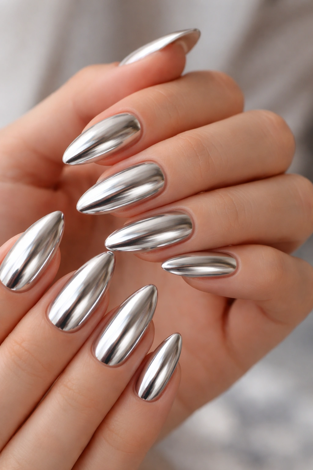 Close-up of hands with chrome almond nails showing a reflective metallic finish.