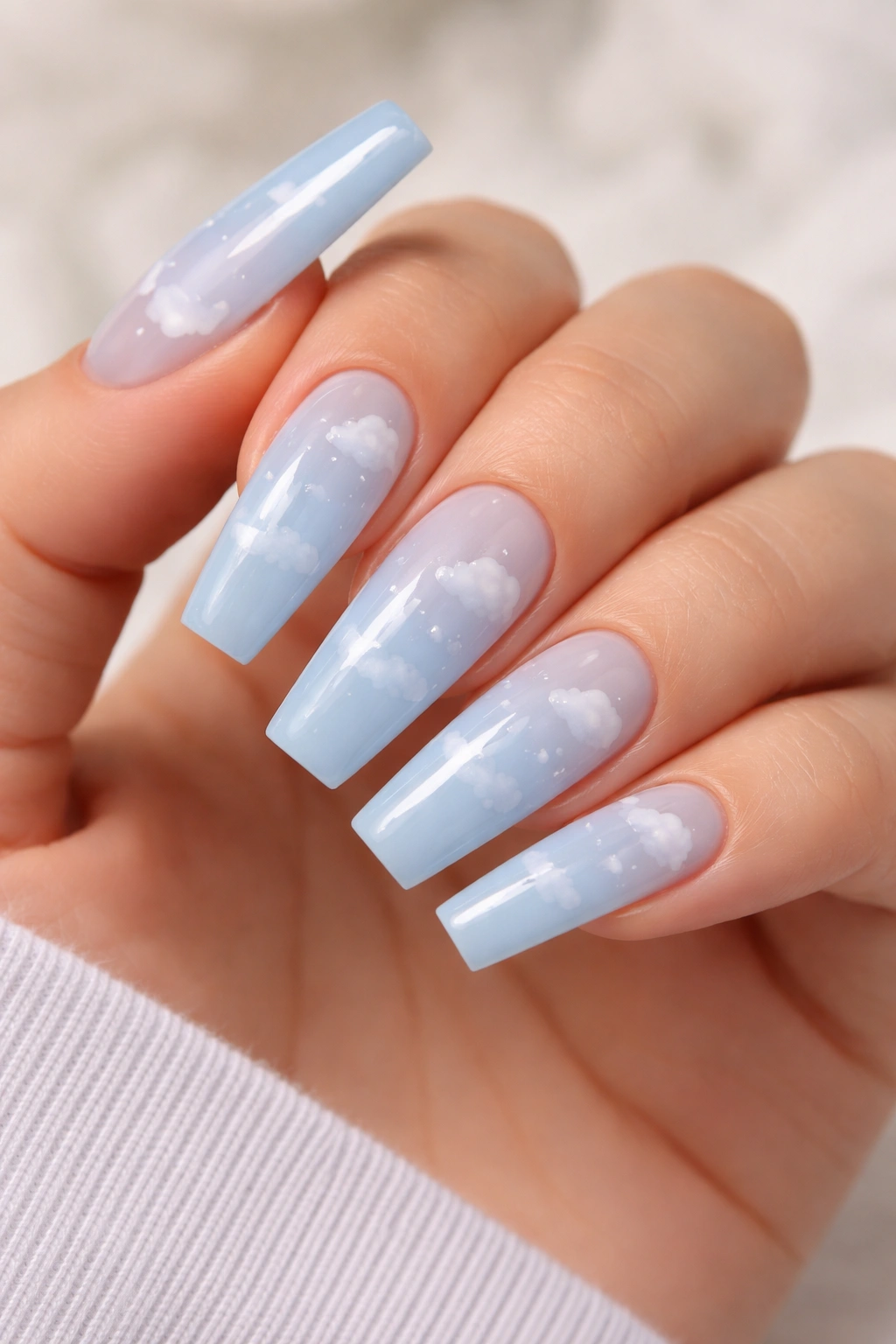 Close-up of blue-and-white cloud coffin nails with a sheer sky-blue base and small white clouds on selected nails.
