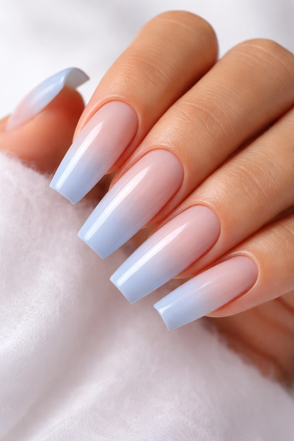 Close-up of coffin nails showing cloudy blue ombre French fade on a milky nude base with a glossy finish.