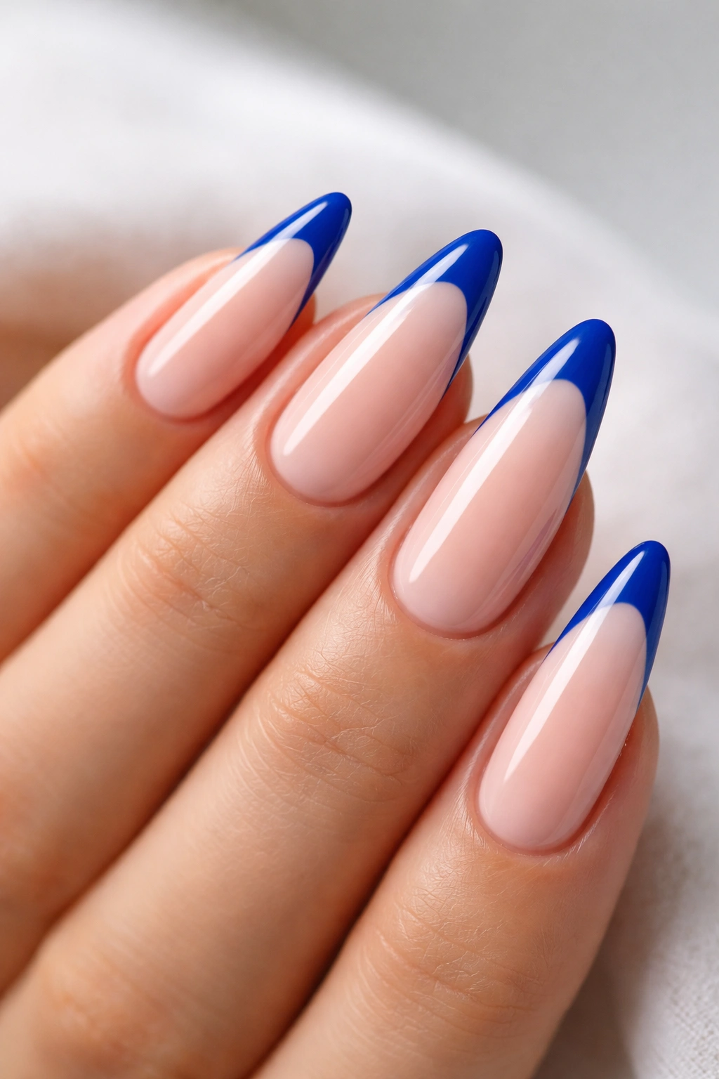 Close-up of almond nails with cobalt blue French tips on a pale nude base