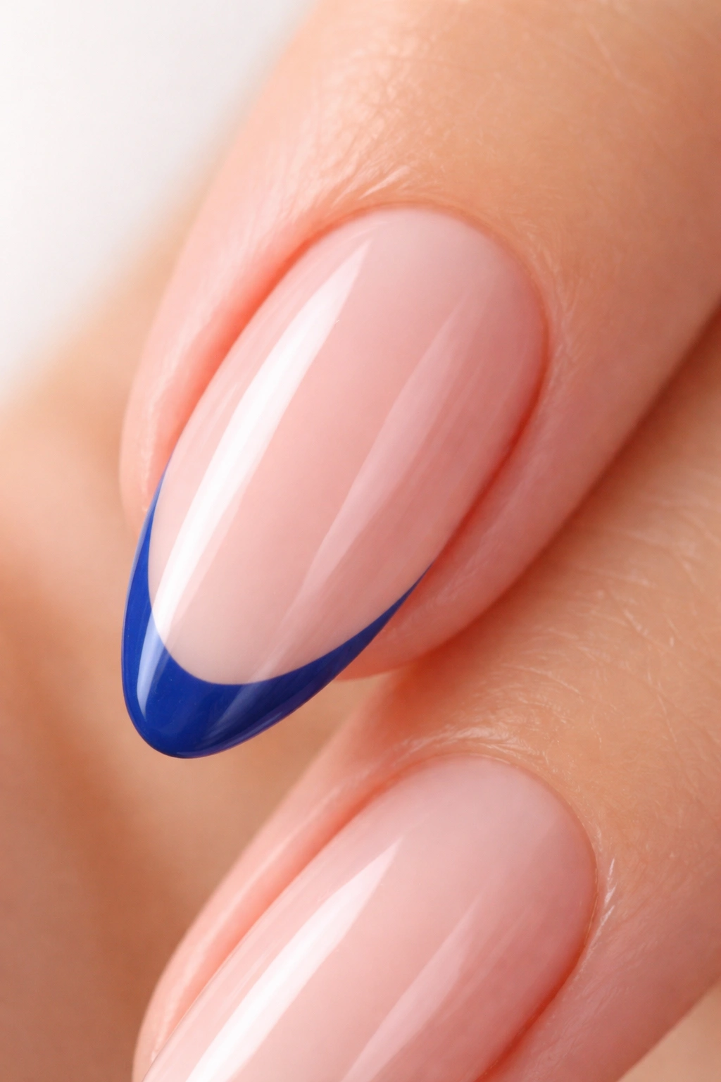 Close-up of an almond nail with a cobalt micro French tip on a sheer pink base
