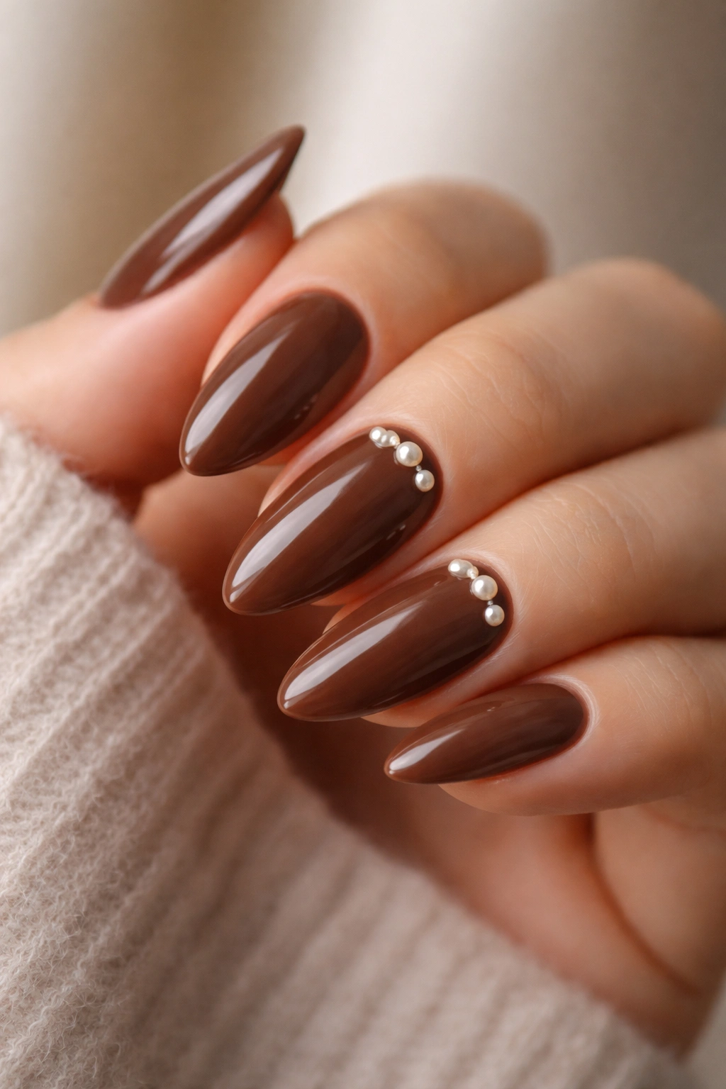 Close-up of cocoa brown almond nails with small pearl accents near the cuticle