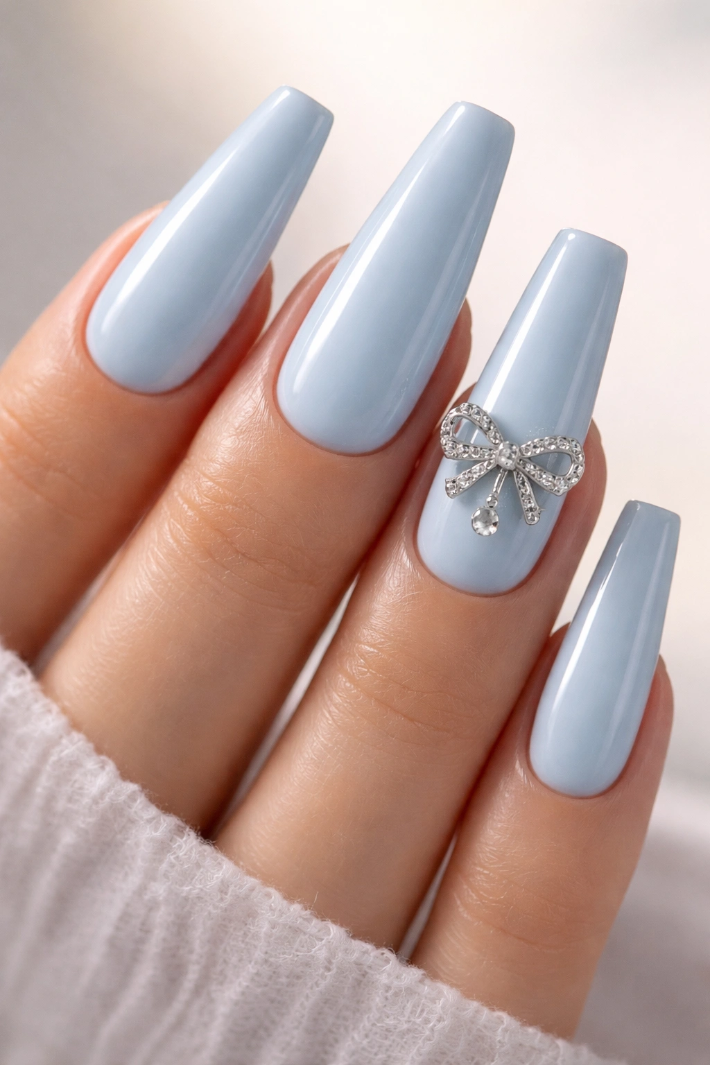 Close-up of baby blue coffin nails with a single silver bow charm on the ring finger