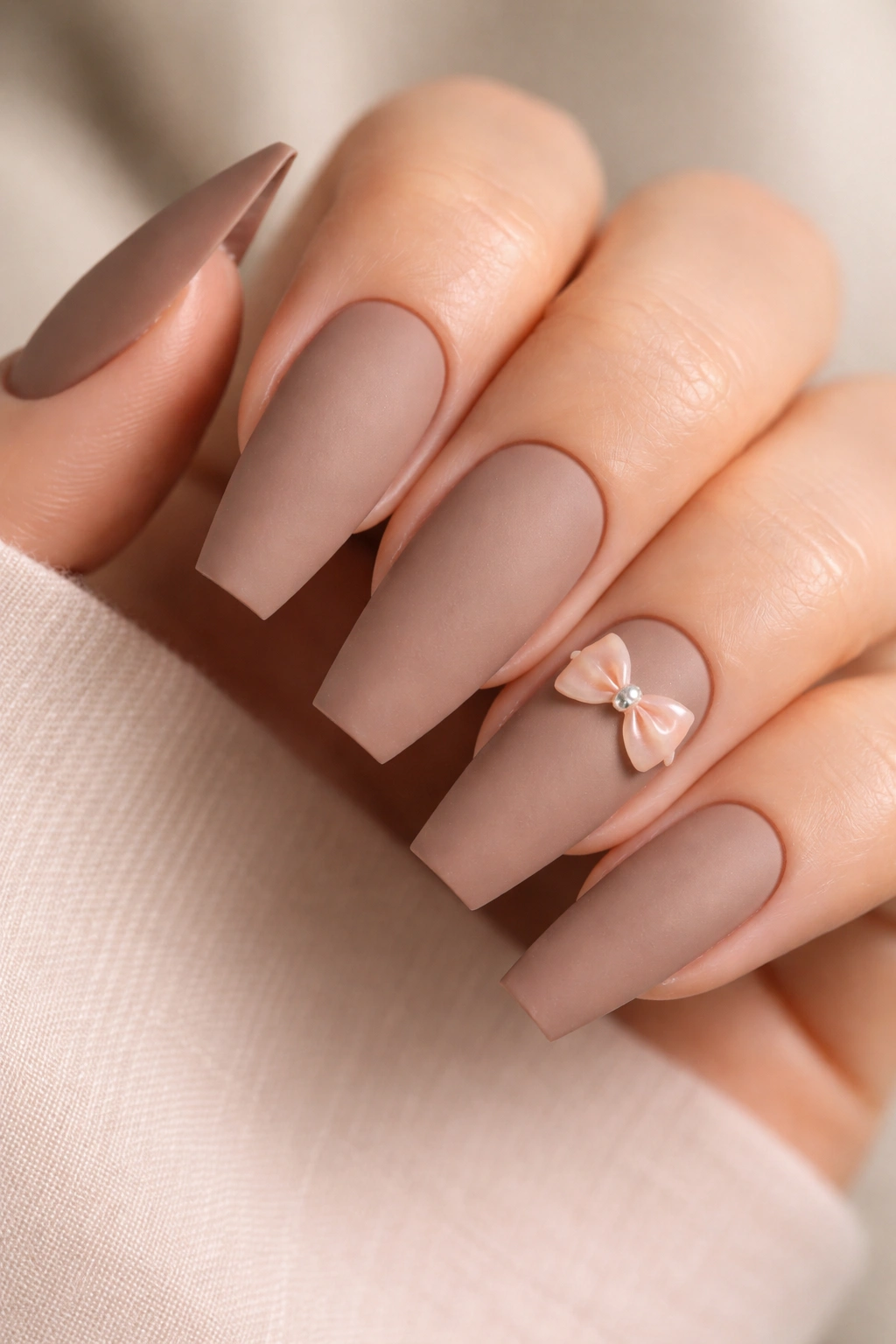 Close-up of matte mocha coffin nails with a glossy bow accent