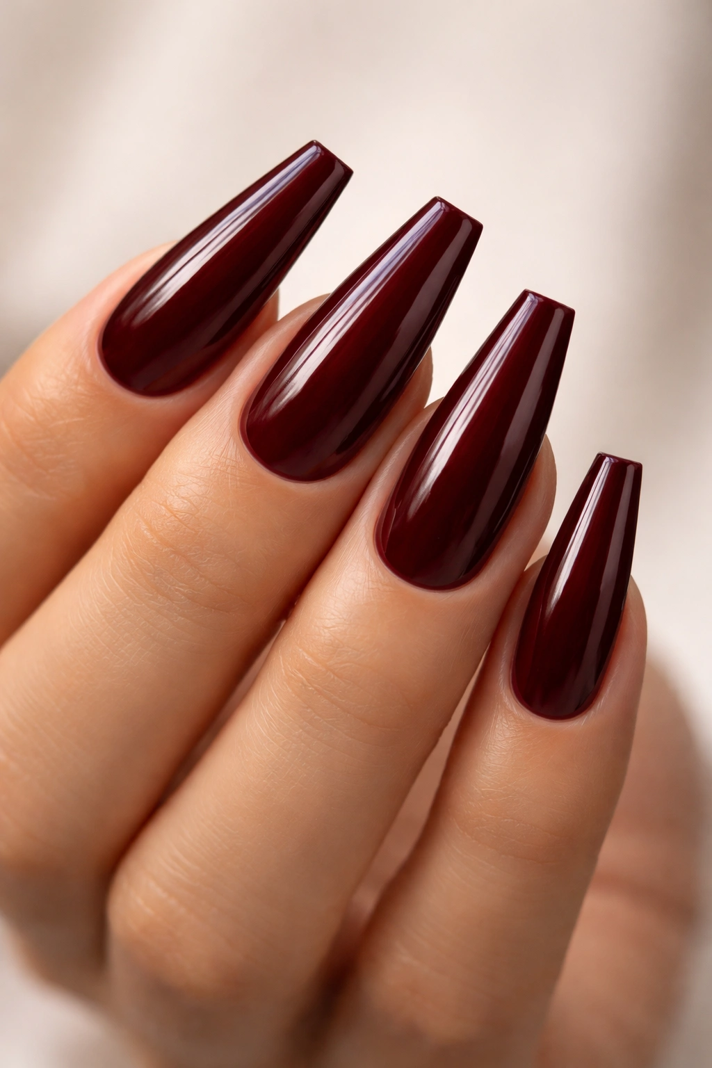 Close-up of coffin-shaped nails in deep oxblood with sharp flat tips on neutral backdrop