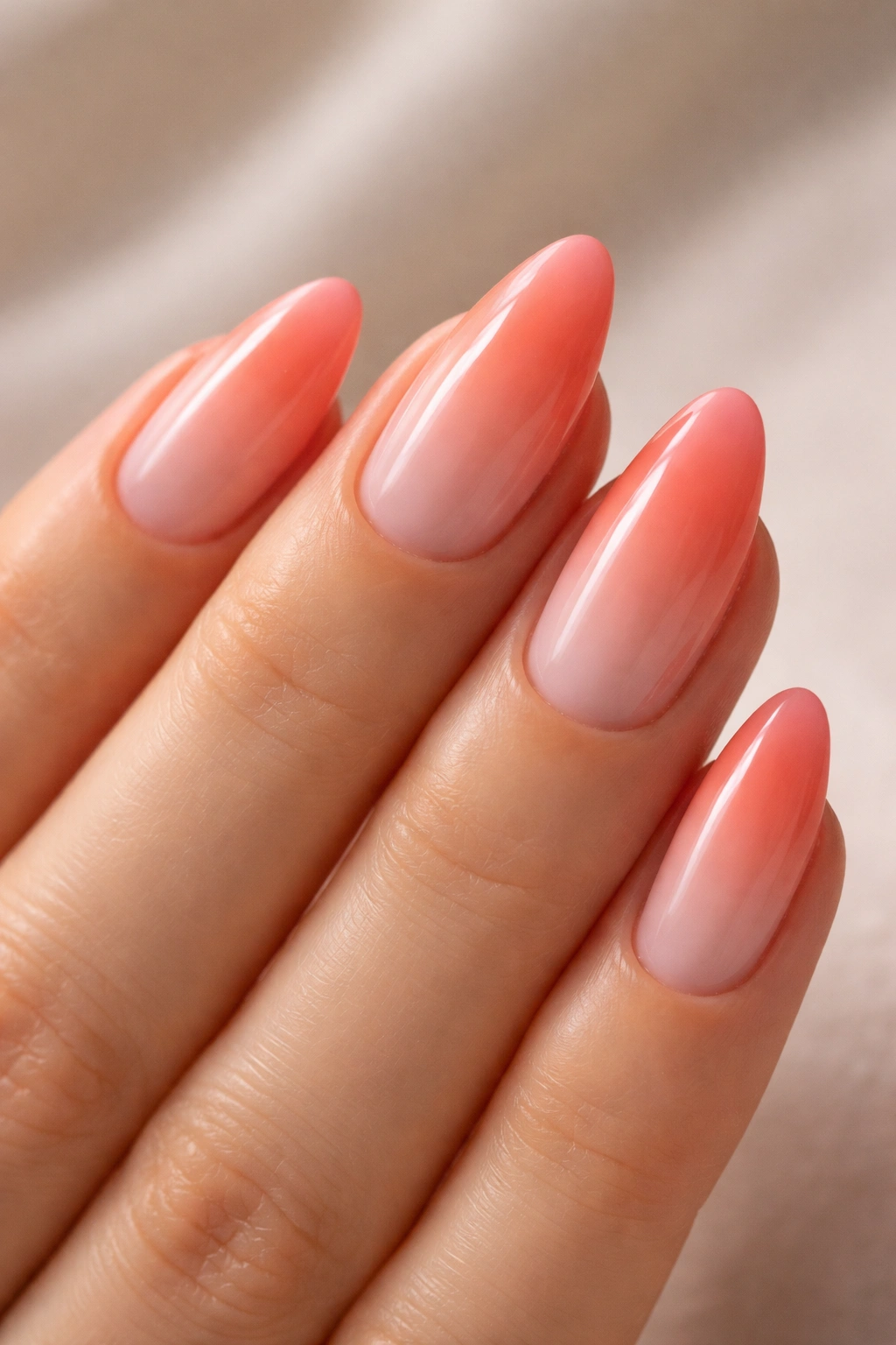 Close-up of coral sunset ombre almonds nails with sheer base