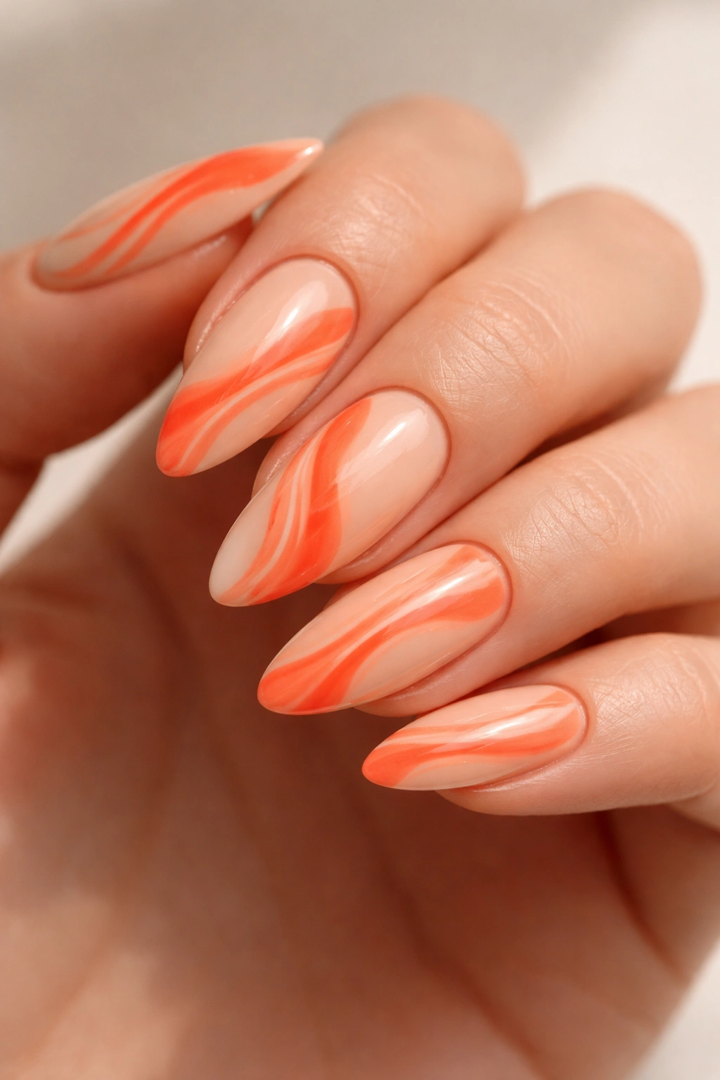 Close-up of coral swirl almond nails with cream base and orange swirl accents