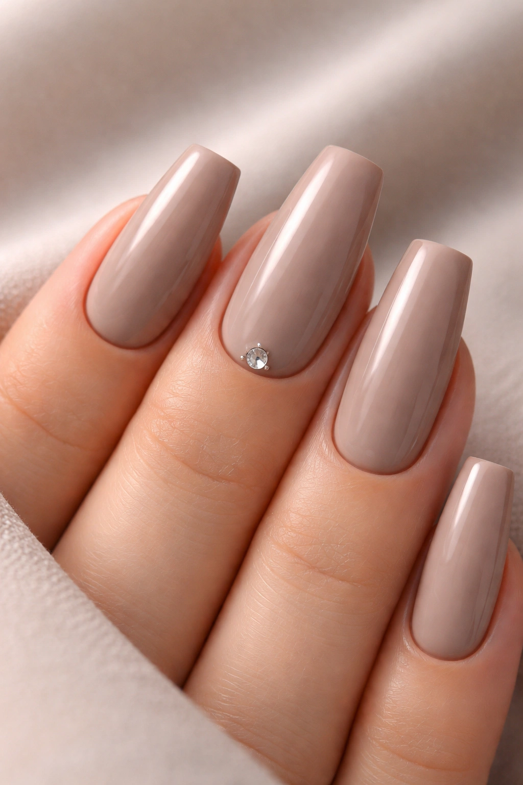 Creamy taupe coffin nails with a single crystal at the cuticle