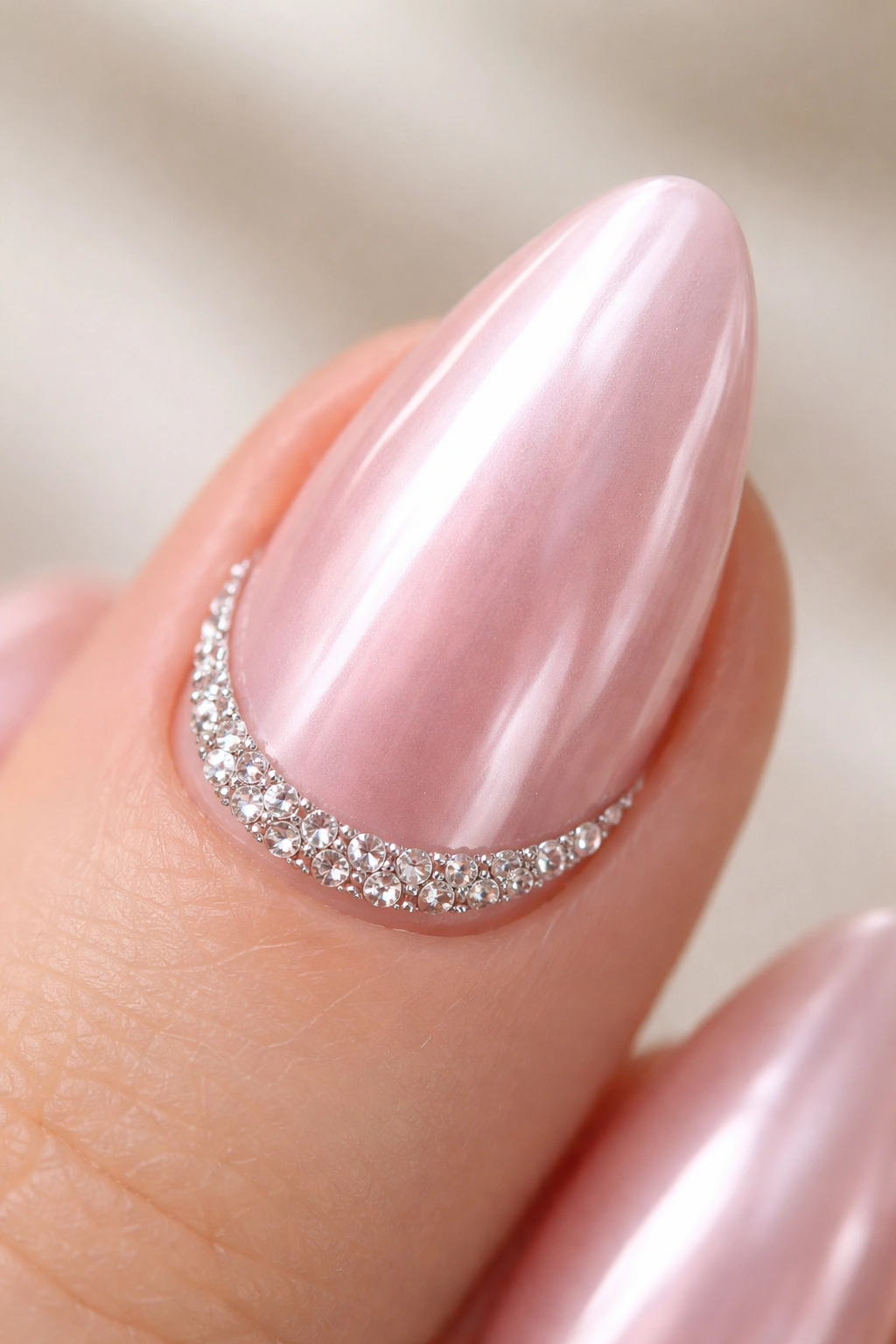 Close-up almond nail with pink chrome and crystal crescent at cuticle.