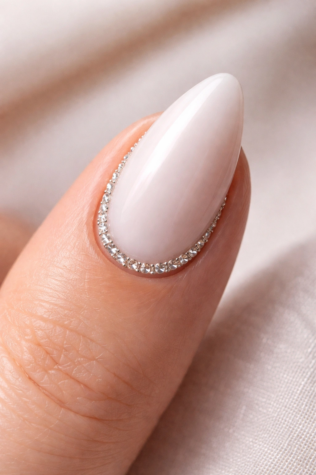 Close-up of a single almond nail with a tiny crystal line along the cuticle on a pale white base