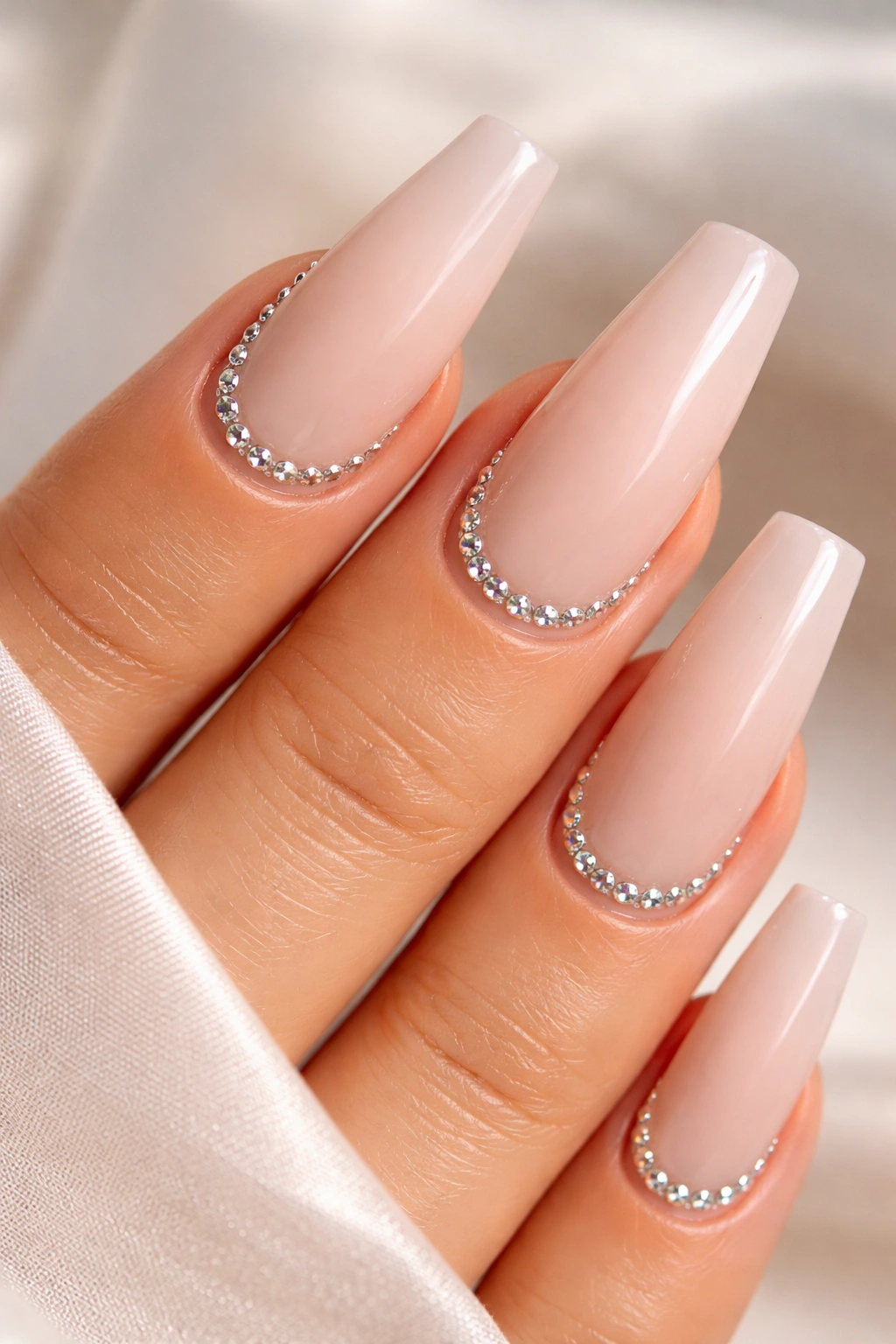 Close-up of nude-based coffin nails with rhinestones along the cuticle