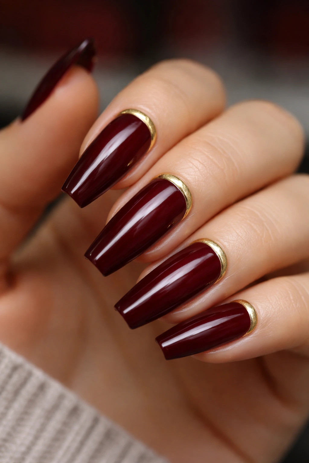 Close-up of dark red coffin nails with a thin gold cuticle cuff along the base