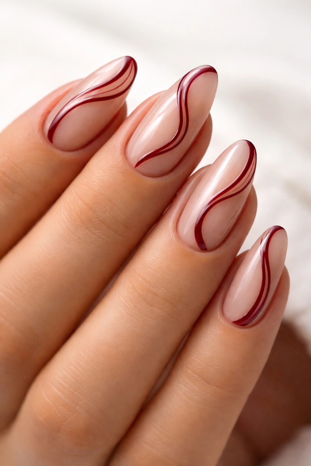 Almond nails with dark red swirls on a sheer base.