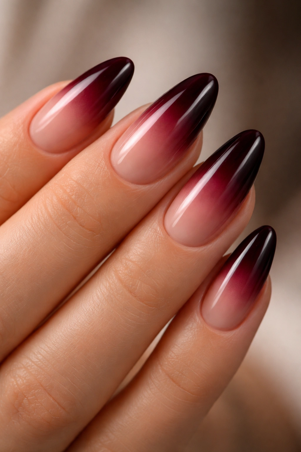 Close-up of almond nails with a seamless burgundy ombré fade on a natural hand