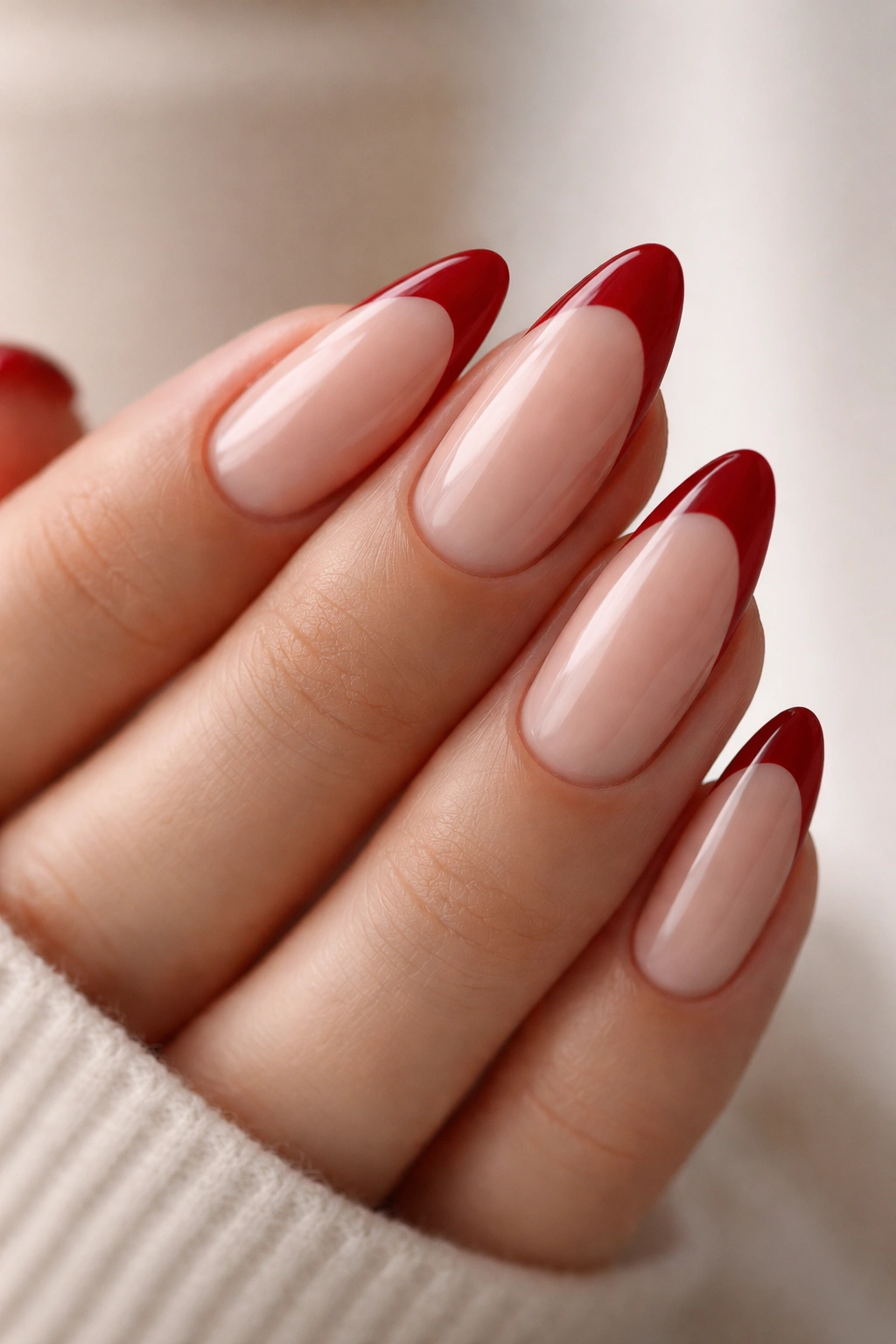 Close-up of almond nails with deep cherry red tips on a milky nude base