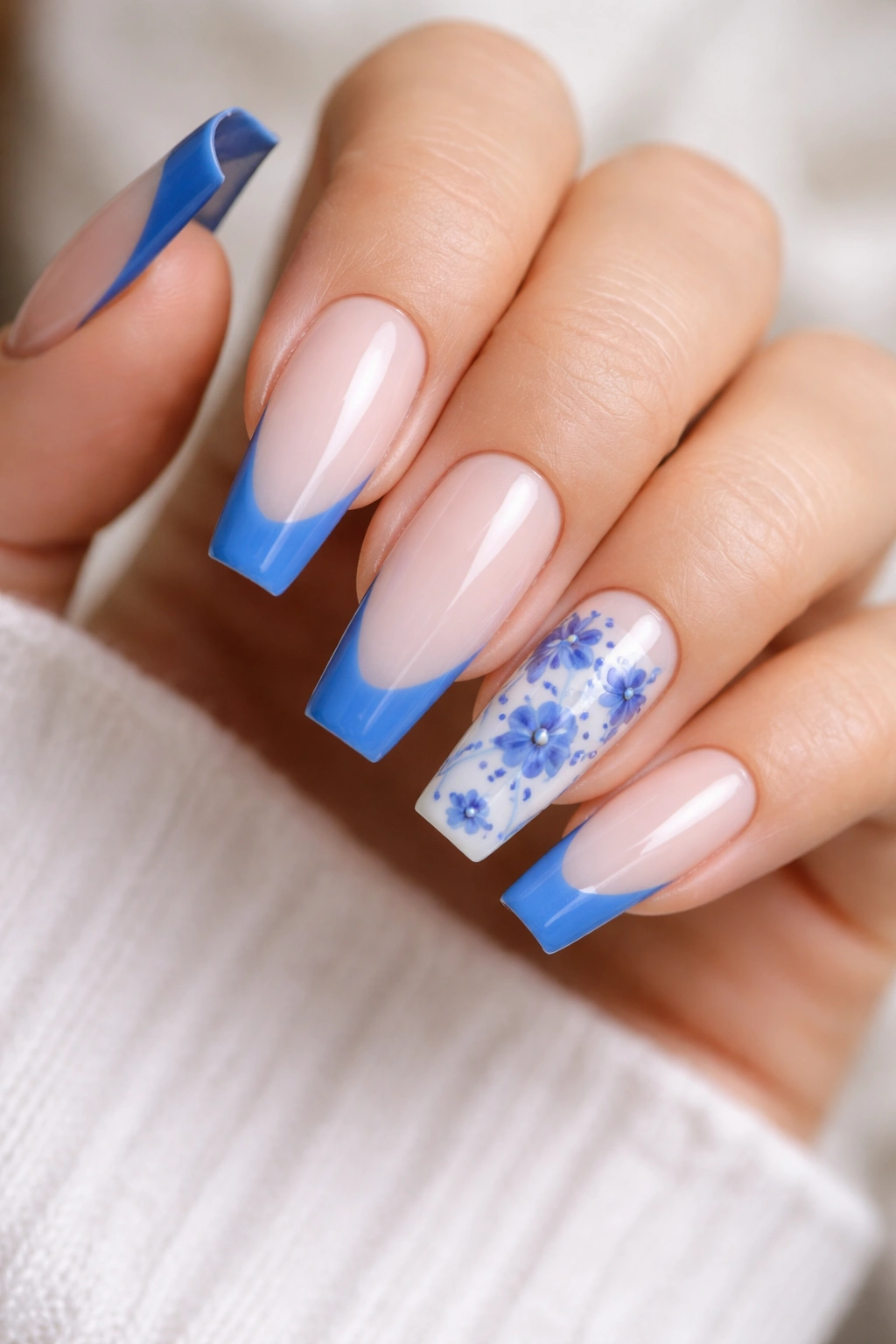 Close-up of Delft blue floral French nails on two accent nails against a sheer nude base.