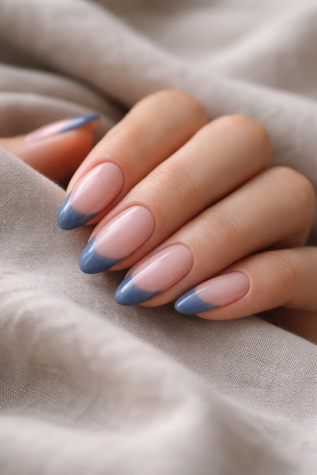 Denim blue French tips on almond nails with satin finish, close-up.