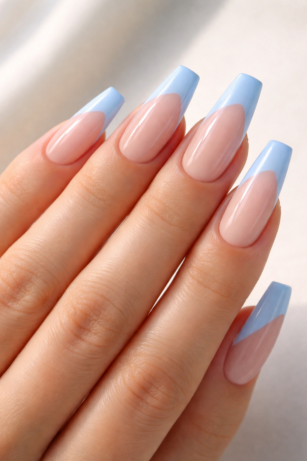 Close-up of coffin nails with diagonal light blue tips on a sheer base.