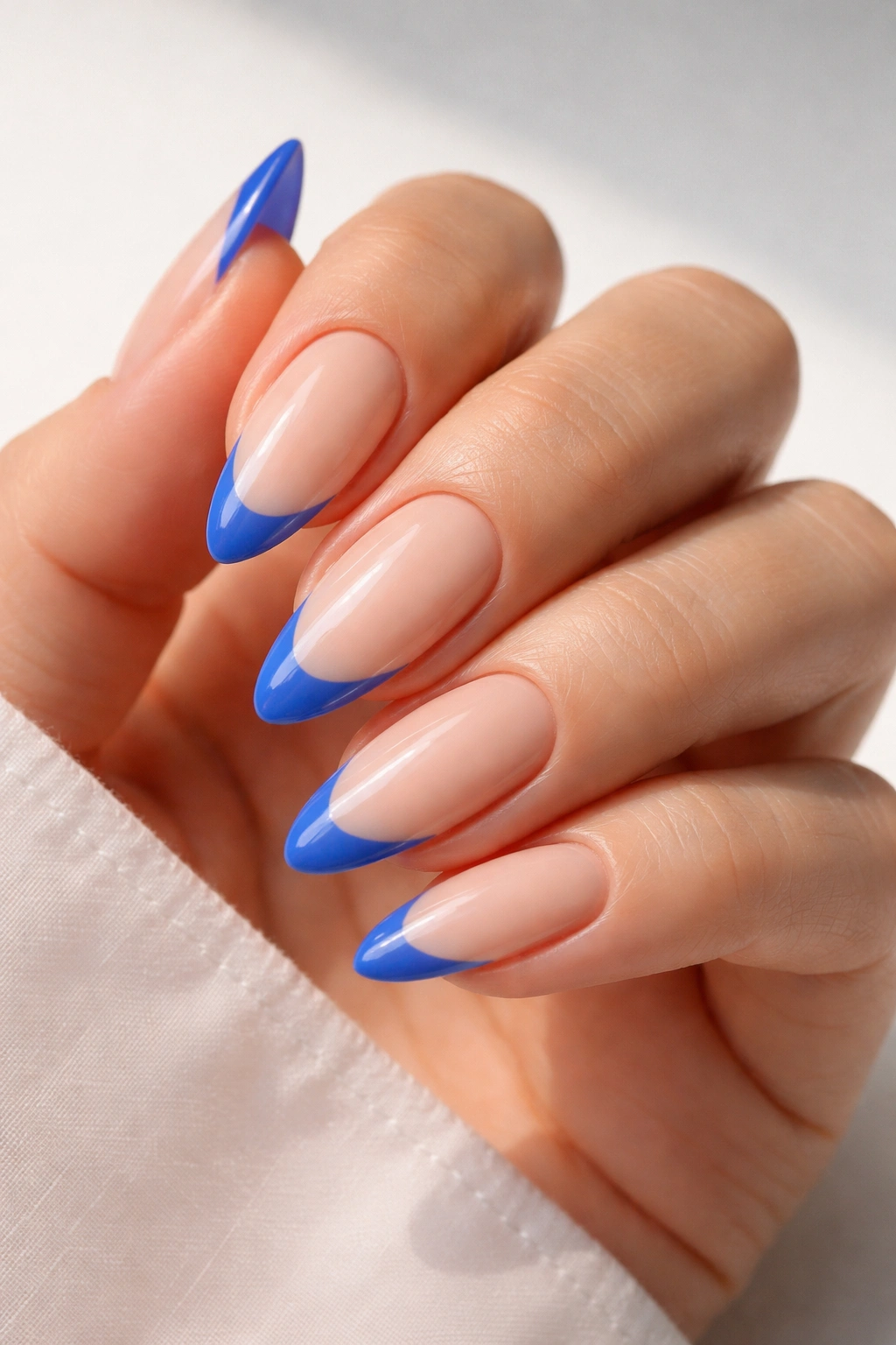 Electric blue tips on nude almond nails with a glossy finish.
